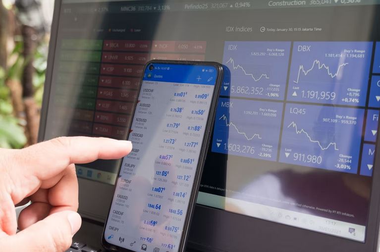 an investor trading forex currency pairs on its smartphone and laptop
